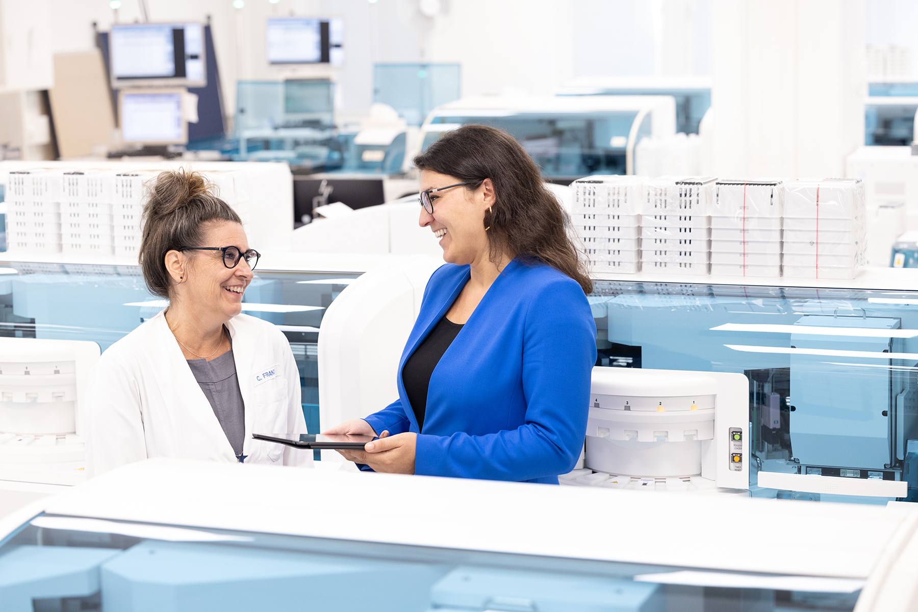 Zwei Frauen um Gespräch im Labor, lachend, authentische Laborfotografie, medizinisches Labor