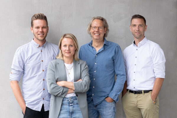 businessgruppenfoto von 4 personen mit schönem lächeln vor einer sichtbetonwand im business-casual look